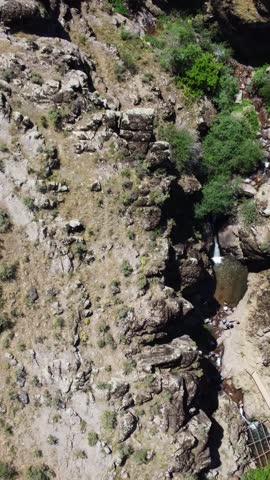 Top down drone shot looking at a mountain stream pool, basalt rock structures and narrow hiking footpaths on parched summer hillsides in Kazakhstan.
