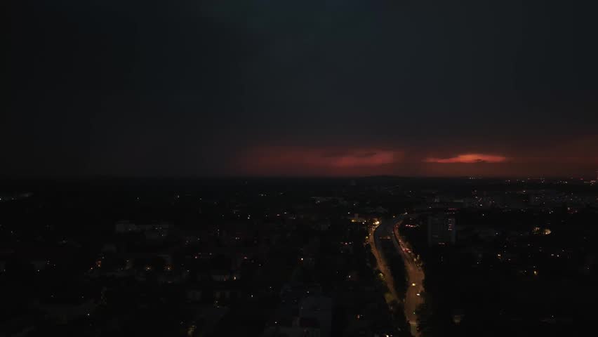 Lightning striking dark stormy sky over city street. Dramatic aerial view drone