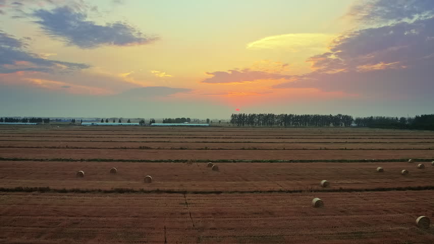 Scenic sunset over rural farmland with hay bales after harvest