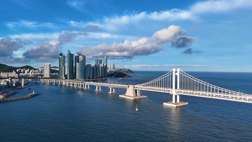 Beautiful aerial view of the gwangan bridge spanning across the blue sea with the modern skyline of busan, south korea, under a cloudy sky