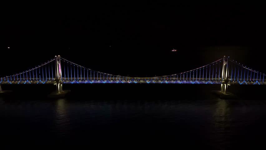 Famous gwangan bridge, also known as diamond bridge, shining with multicolored lights over the dark water in busan, south korea