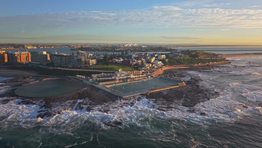 Aerial sunrise establishing of Newcastle Ocean Baths surrounded by surf and coastline, drone NSW Australia