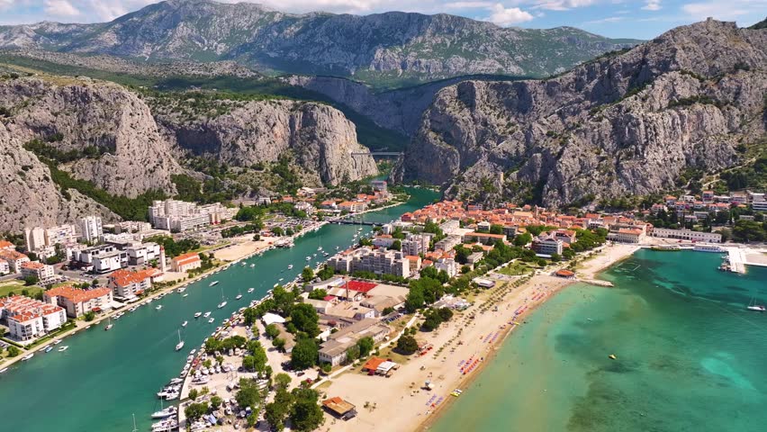 Omis features a coastal view with a sandy beach and fishing boats. The town includes buildings along the waterfront. Mountains surround the area.