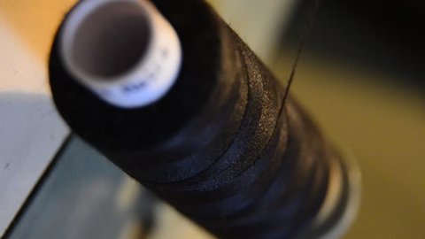 spool of black thread with needle stuck. Unrolls during process of sewing on machine in clothing industry production, Extreme close up, selective focus.