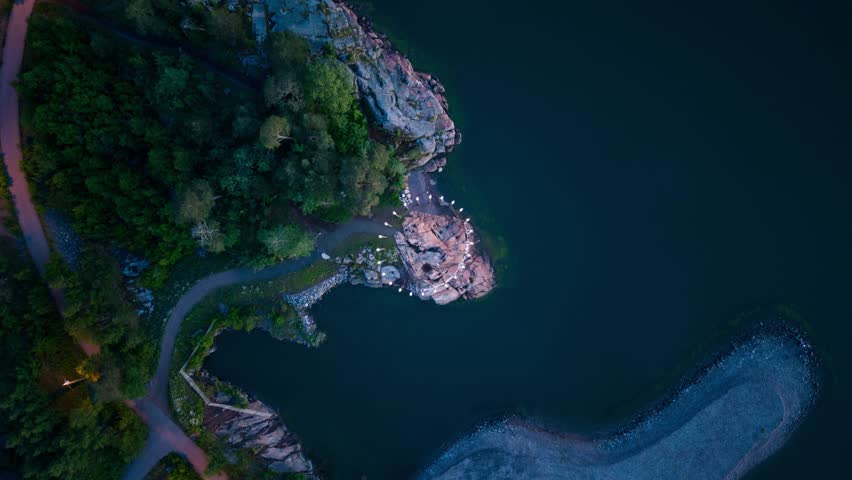 Aerial view of the rocky coastline and forested paths of Kruunuvuorenranta at dusk in Helsinki, Uusimaa, Finland.