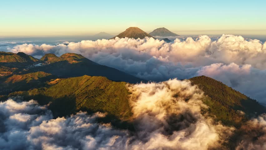 Aerial view of Sindoro Sumbing mountains surrounded by thick clouds at sunrise in Kecamatan Kedu, Jawa Tengah, Indonesia.