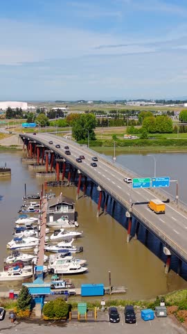 Richmond, British Columbia, Canada - An Aerial View of a Bridge Crossing a River Beside a Marina with Docked Boats, Surrounding Roadways, and Airport-area Landscapes - Vertical Shot