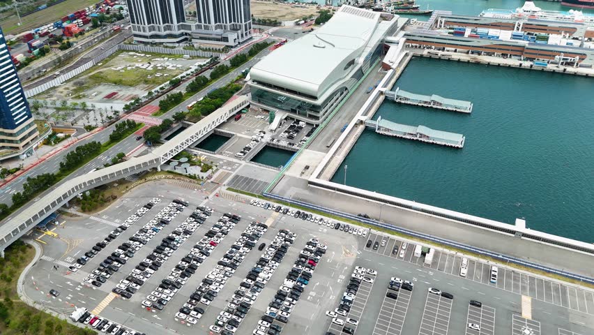 Aerial view of the modern Busan Port International Passenger Terminal with its curved roof, adjacent parking lots, and ferry piers extending into the harbor in Busan, Busan, South Korea.