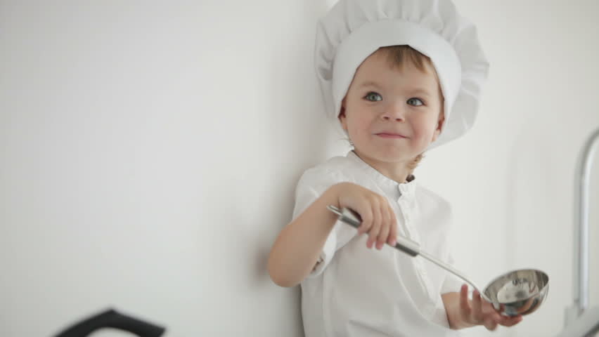 Little cook with ladle sitting on table and laughing
