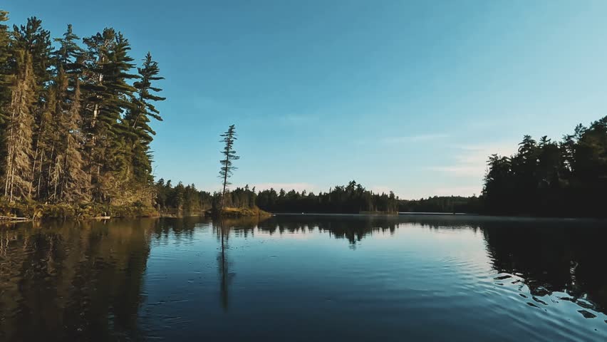 A stunning 4K scene of a remote lake with reflecting water and silhouetted trees in Temagami, Ontario, Canada at sunset