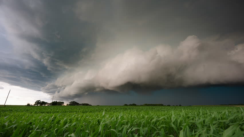 A towering supercell storm moves across open green fields, showing rotating cloud structure, dramatic severe weather, rural landscape, powerful atmosphere, and intense thunderstorm development.