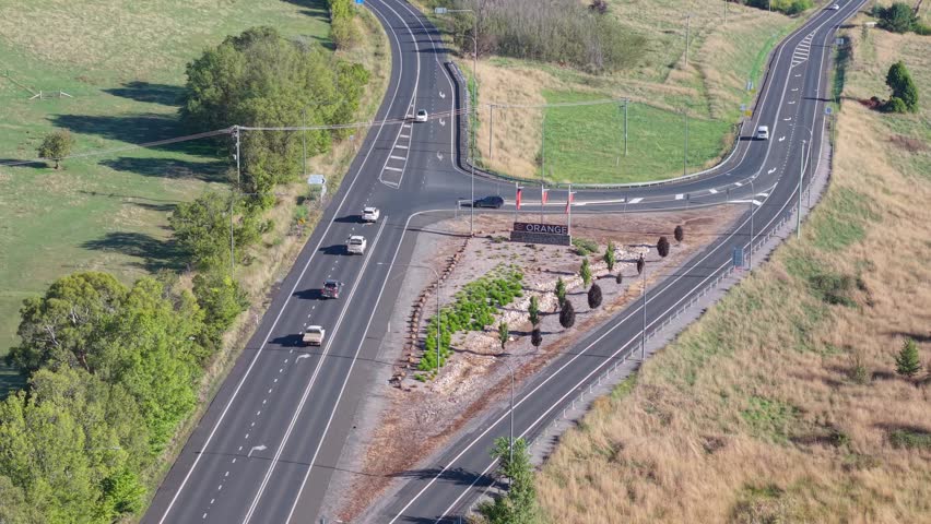 Drone aerial view of the Orange town sign and Mitchell highway intersection in regional New South Wales, Australia, with vehicles, landscaped median and rural scenery.