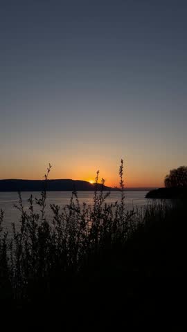Scenic landscape view of a peaceful lake at dusk with the sun dipping below the distant horizon hills.