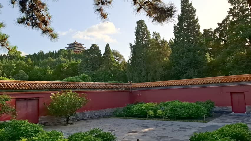 Scenic view of Jingshan Park in Beijing, China. Traditional red wall with tiled roof, lush green trees, ancient Chinese pagodas standing on top of hill under a blue sky. Beautiful oriental landscape 