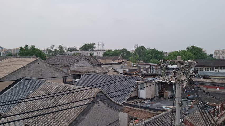 Overhead view of traditional Chinese hutong rooftops with grey tiles under an overcast sky in Beijing. Authentic ancient courtyard houses architectural landscape. Beautiful cultural heritage scene