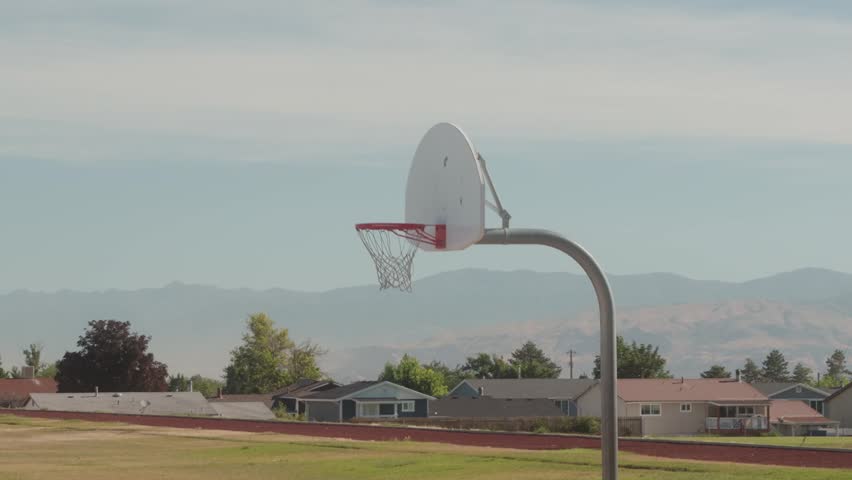 Still view of outdoor basketball hoop near track and mountains.