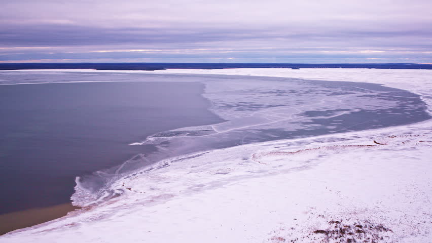 Drone footage of a remote Lake Superior bay partially covered in ice with a peaceful winter foreground.