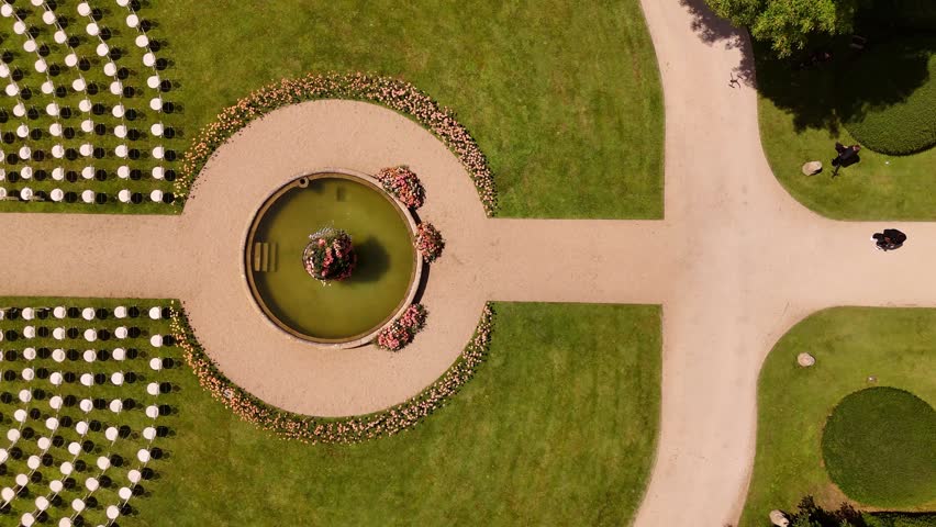 Elegant outdoor wedding ceremony on a large manicured lawn with symmetrical landscaping, a fountain, and a floral-lined aisle leading to a ceremony platform surrounded by fresh flowers