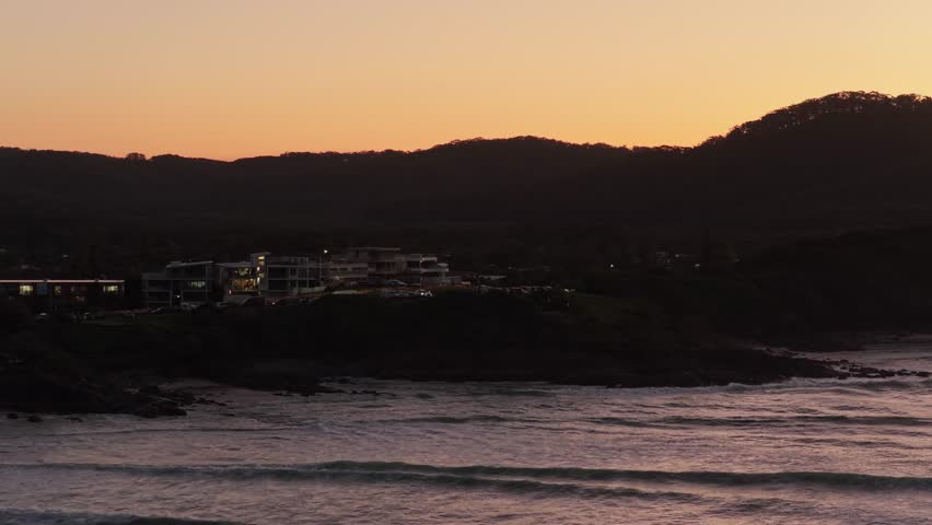 Slow aerial tracking view moving from right to left along Cabarita Beach at twilight with the Wollumbin Mount Warning hinterland in New South Wales, Australia