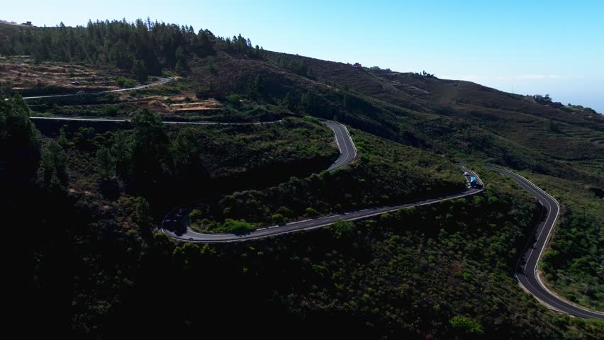 Bus drives along winding mountain road through volcanic terrain and green hills