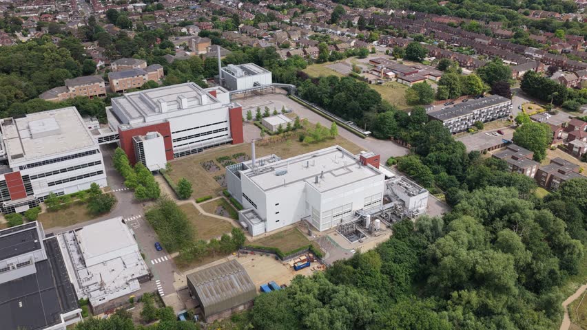 A wide aerial shot captures the impressive complex of modern white and red buildings, surrounded by lush green trees and well-maintained lawns.