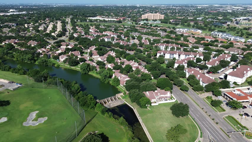 Elm Fork Trinity River meanders through Irving, Texas separating golf course fairways from mature residential neighborhoods. Spillway infrastructure sits amidst canopy trees paved arterial roads. USA