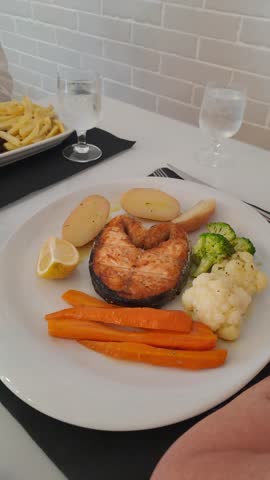 Cooked salmon steak served with boiled potatoes, carrots, broccoli and cauliflower on a white plate