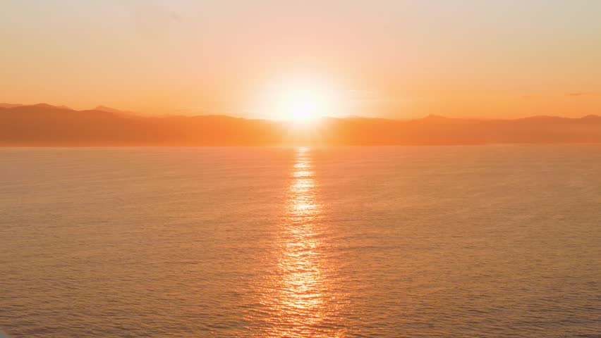 Wide angle view of a brilliant bright sun rising over a peaceful coastal marine channel