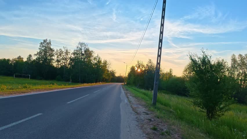 Country road stretching into sunset through forest roadside. POV bicycle ride.