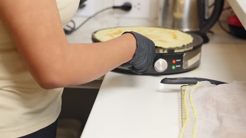 Professional chef wearing black gloves carefully placing slices of cheese onto a freshly made crepe, preparing a high protein savory meal