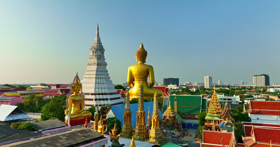 A striking aerial view of Bangkok featuring a golden Buddha statue and a white stupa surrounded by colorful temple rooftops, set against the backdrop of the modern city skyline.