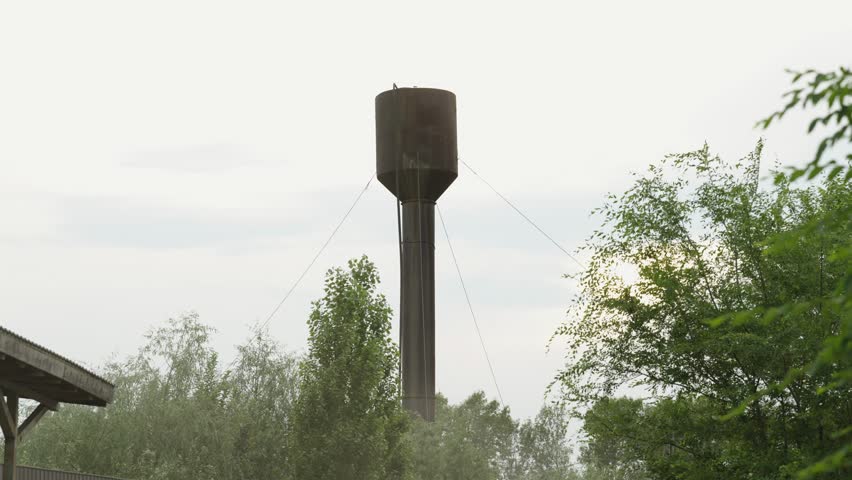 Old metal water tower rising above green trees against sky