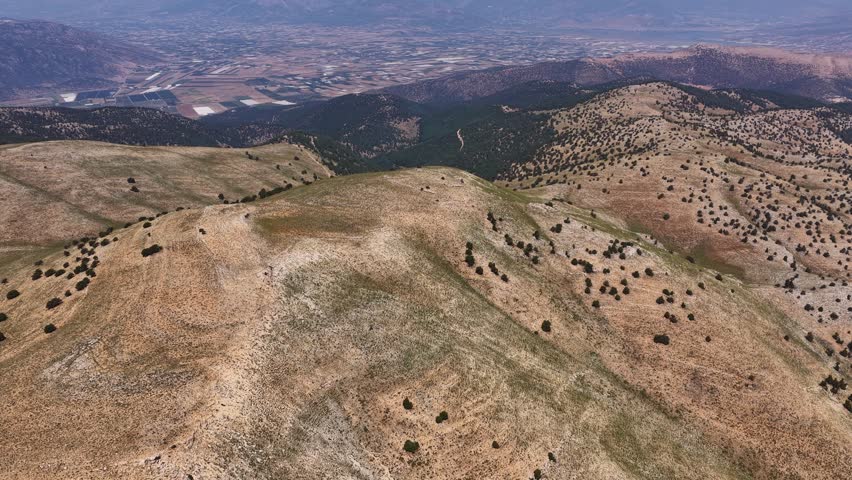 A sweeping drone view stretching from the high hills to the agricultural plain in the distance.