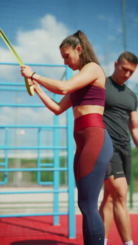 A determined woman engages in an outdoor workout, using resistance bands for strength training. She performs a fitness exercise with dedication on a sunny day.