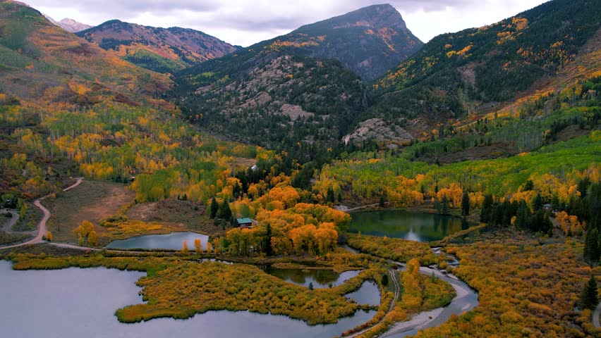 Expansive aerial view of Colorado mountain valley with golden aspen trees, alpine lakes, and a river.