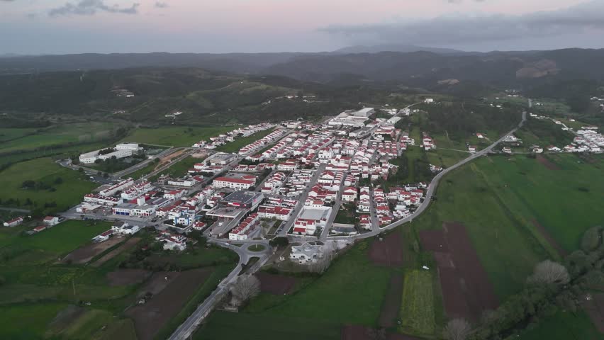 Aerial drone push in shot revealing Aljezur, Portugal, a charming town surrounded by lush green hills under a cloudy sunset sky. Part of the Rota Vicentina, and Fisherman