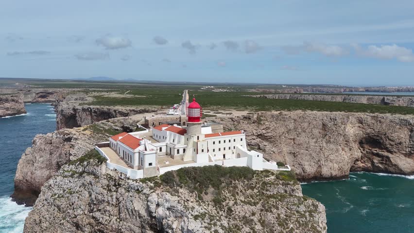 Aerial drone pan right and tracking shot of the iconic Cabo de São Vicente lighthouse on rugged cliffs in Sagres, Portugal. Part of the Rota Vicentina, Fisherman