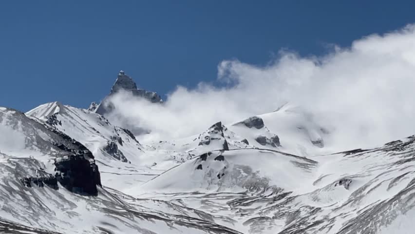 A breathtaking panoramic view showcases the majestic snow-capped peaks of the Tibetan Plateau. Clouds gracefully drift across the rugged mountains, creating a stunning high-altitude landscape under