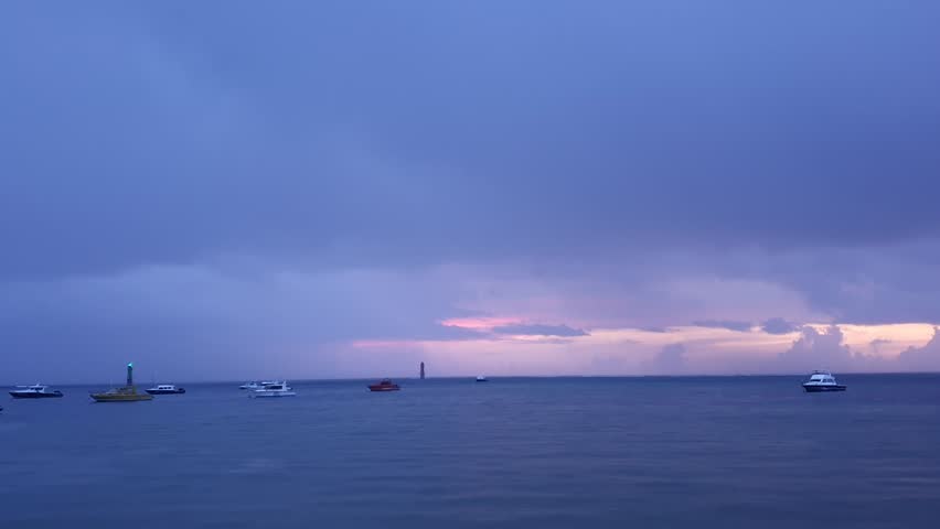 Wide shot of a calm tropical sea under a dramatic dark overcast sky with heavy storm clouds during twilight or dawn.