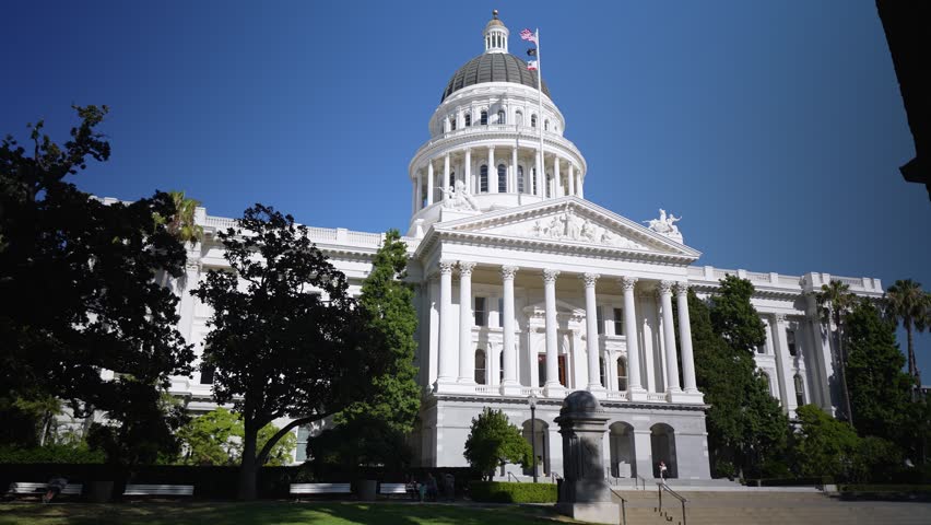 California State Capitol in Sacramento shows clear blue skies and bright sunlight as visitors walk near the historic government building