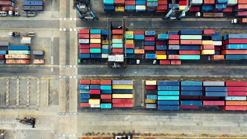 Drone aerial view of colorful shipping containers neatly arranged at a busy logistics terminal.