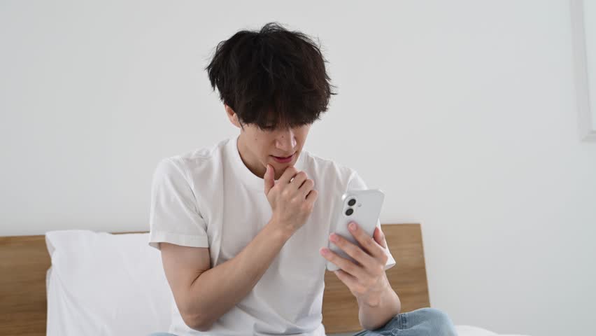 Japanese Man in His Thirties Looking Worried While Using a Smartphone