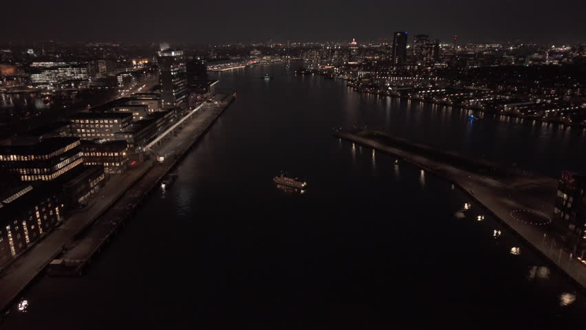 Night aerial view of a city river with lit bridge, office buildings, and skyline reflections in dark water