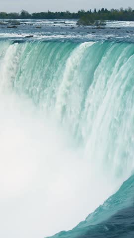 Powerful waterfall pours over curved rock edge, turquoise water dropping into mist below, forested horizon above, continuous river flow across frame sequence, strong motion, natural texture