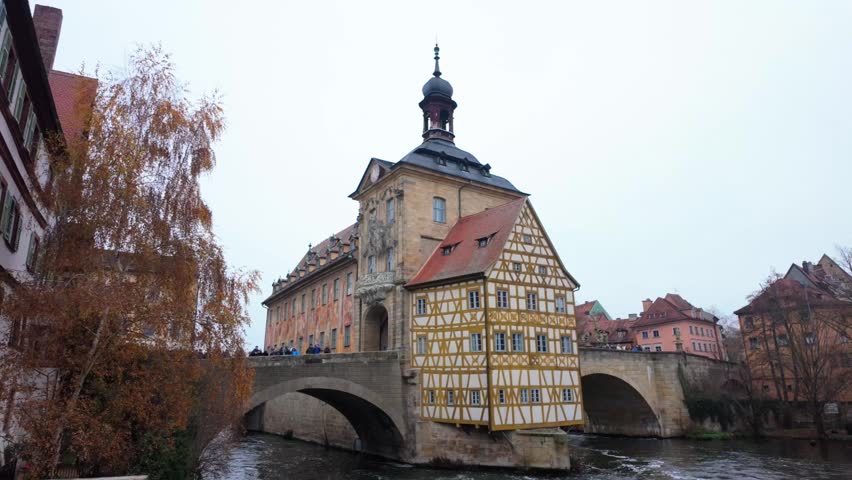 Female tourist with a mobile phone capturing the iconic altes rathaus, the old town hall, over the regnitz river in bamberg, germany during a cloudy autumn day revealing the landmark