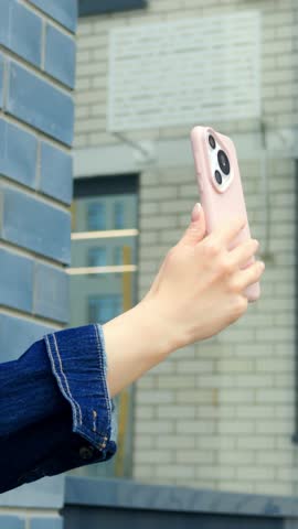 Urban female model with casual style. Young Caucasian woman standing against brick wall with smartphone. Stylish young woman of Caucasian descent posing with mobile device on city rooftop