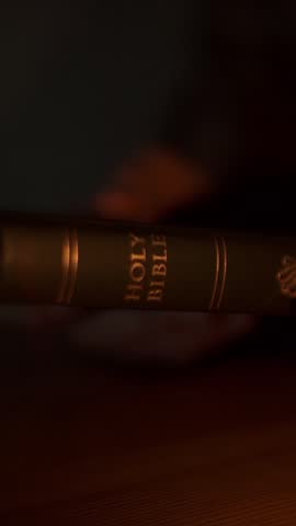 Close-up of a person opening the Holy Bible on a wooden table in a dimly lit room