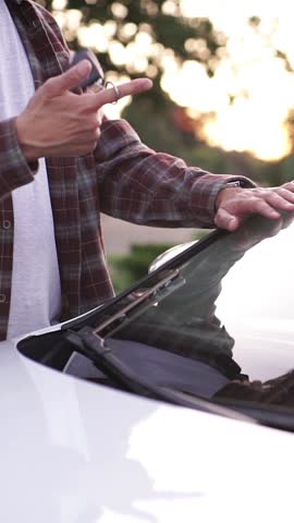 Man twirling car key fob on his finger next to a white vehicle at sunset, lifestyle concept