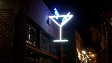 Shot of a neon martini glass sign on a tavern at night. Features a bright green olive and blinking blue bubbles.