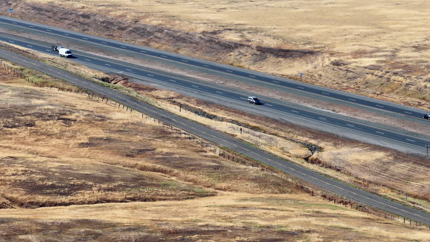 Aerial Flyby View of a Rural Highway Crossing Dry Golden Grassland on a Clear Day